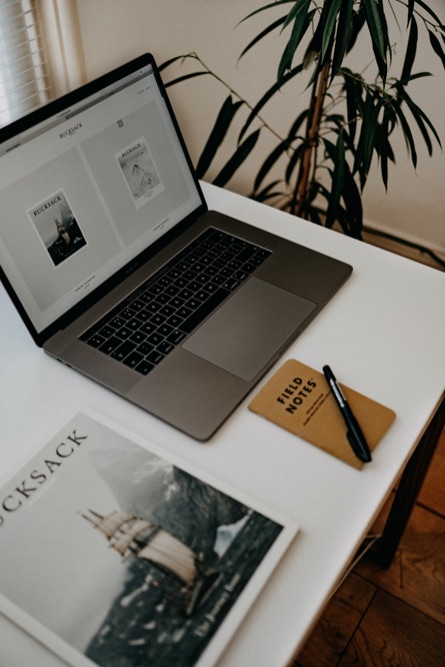 Bureau blanc avec un ordinateur, un carnet, un livre et un stylo